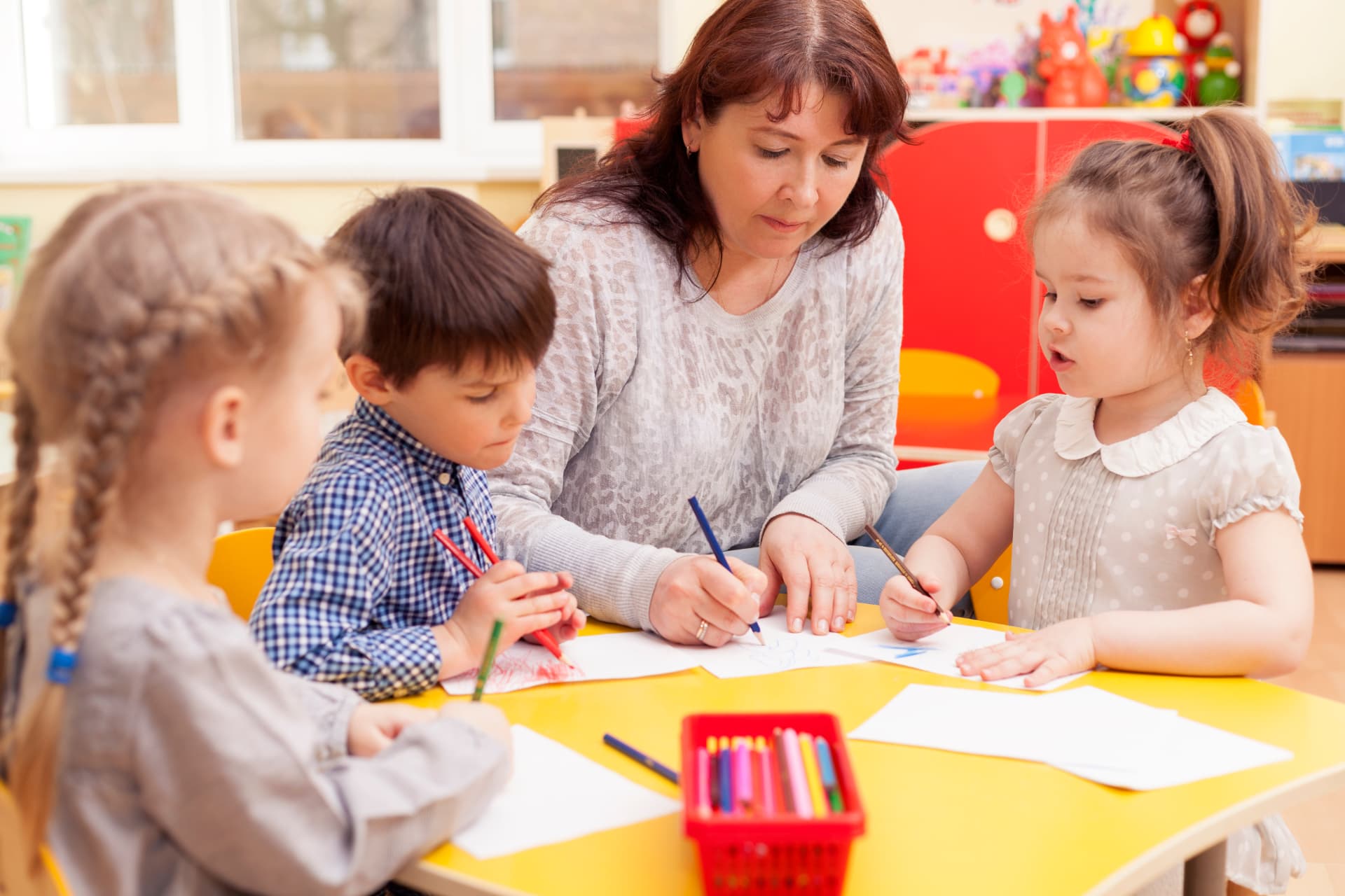 A teacher guiding preschool children through a drawing activity